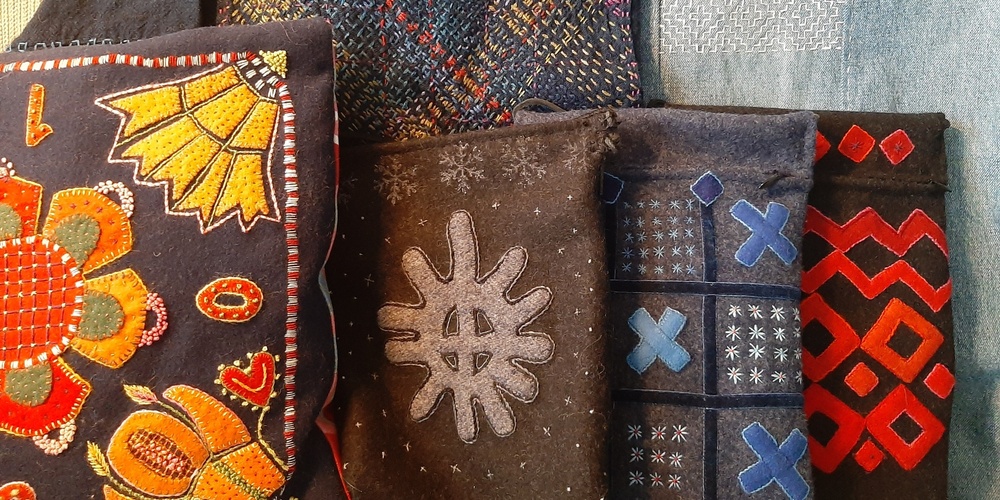 Flera textilier med färgglada broderier och mönster, inklusive kuddar och väskor, visas tillsammans.