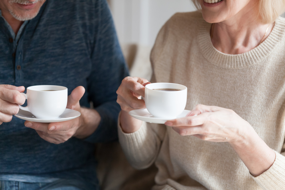 Två personer sitter tillsammans och håller vita kaffekoppar, leende och samtalande.