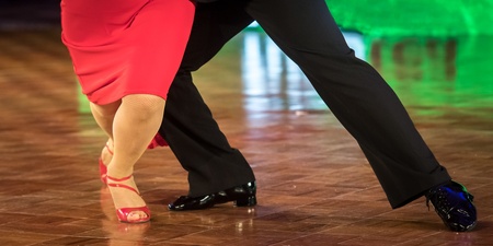 Två personer dansar tillsammans på ett dansgolv, endast deras ben och fötter syns.