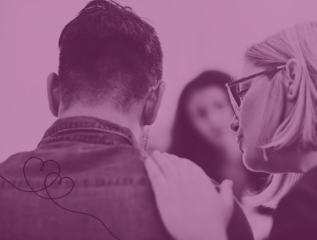 En person lägger en hand på en annans axel i en stödjande gest, med en tredje person i bakgrunden.