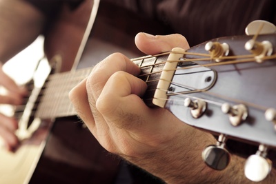 Närbild av en person som spelar akustisk gitarr, fokus på vänster hand på gitarrens greppbräda.