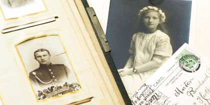 Ett gammalt fotoalbum, ett porträttfoto av en flicka, vykort och ett fickur i guld på ett bord.