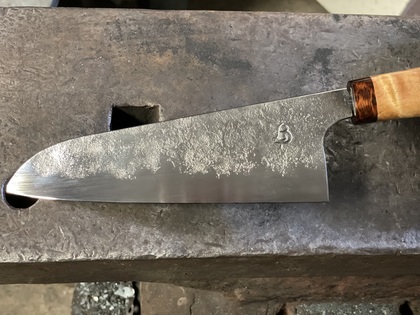 En handgjord kockkniv med trähandtag ligger på ett smidesstäd.