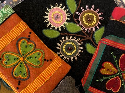 Färgglada broderier med blommor, hjärtan och ett fyrklöver på tygbitar i olika färger.