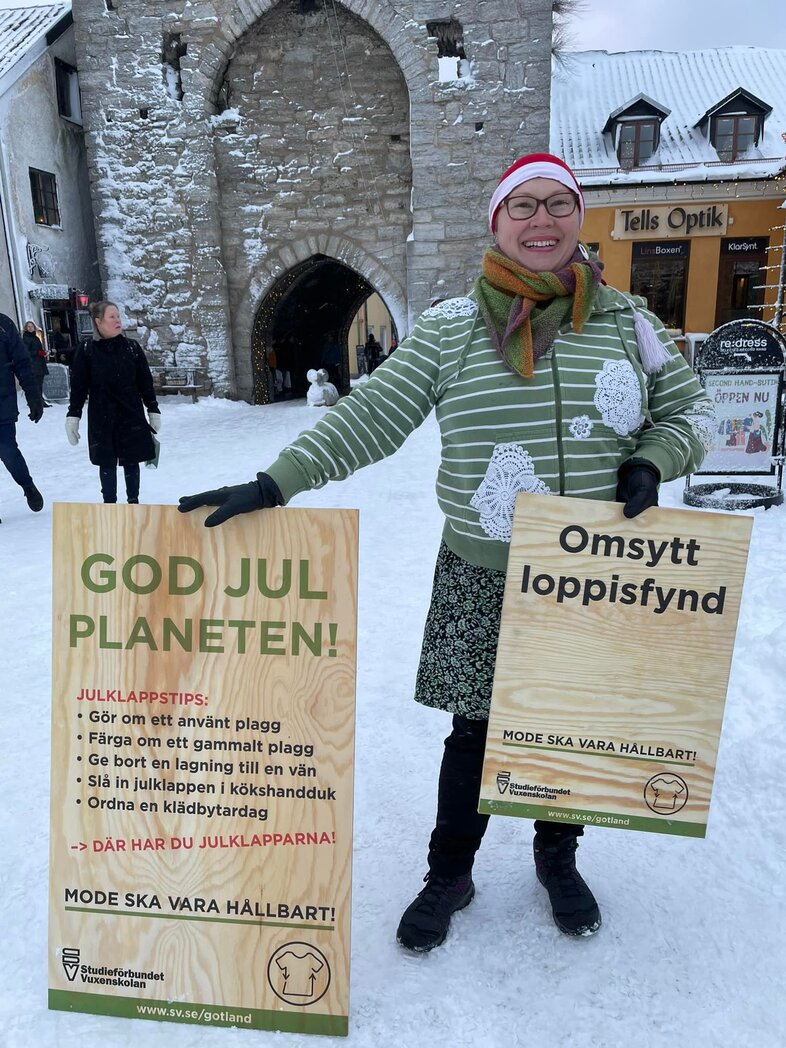 Person i randig tröja och tomteluva står i snöig stadsmiljö och håller skyltar om hållbara julklappstips.
