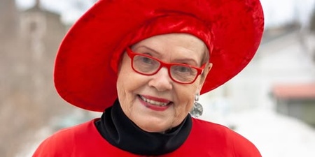 Person klädd i röd mantel och stor röd hatt står utomhus på vintern.