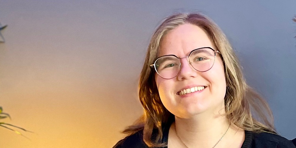 Två leende personer sitter tillsammans i en blå soffa i ett rum med blå vägg och grön växt.