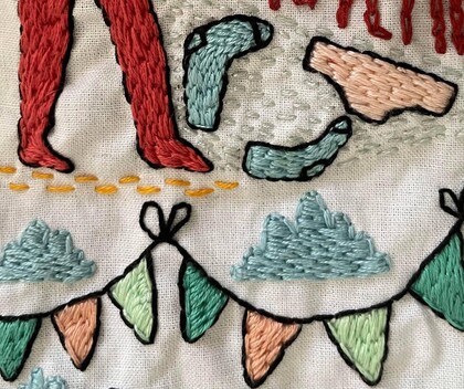 Närbild av broderi med färgglada vimplar, kläder och ben på vit bakgrund.