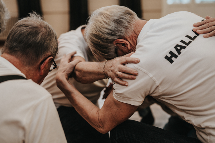 Flera äldre personer sitter i en cirkel och håller varandras armar i en stödjande gest.