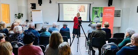 En kvinna håller en presentation inför en sittande publik i ett ljust konferensrum.