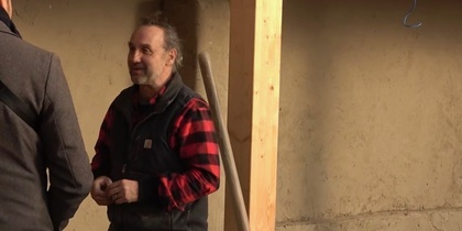 Två personer samtalar inomhus, en bär röd- och svart-rutig skjorta och väst, ansikten är suddade.