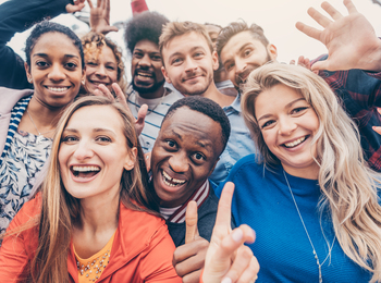 En grupp glada unga vuxna står tätt tillsammans och ler mot kameran utomhus.