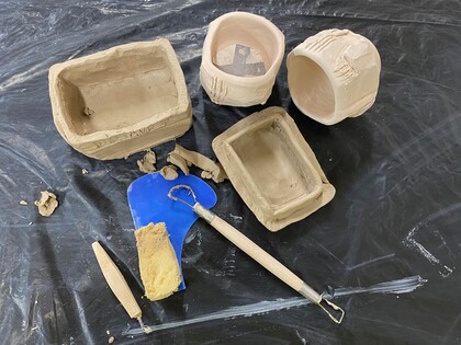 Flera ofärgade keramikskålar och verktyg ligger på ett svart underlag, redo för bearbetning.