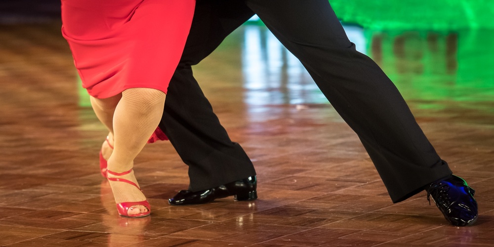 Två personer dansar tillsammans på ett dansgolv, endast deras ben och fötter syns.