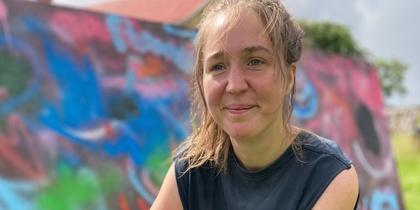 En kvinna sitter på huk på gräs framför en färgglad graffitivägg utomhus.