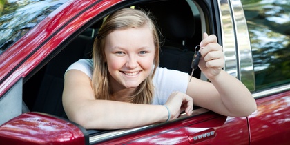 Ung kvinna sitter i en röd bil och håller upp en bilnyckel med ett leende.