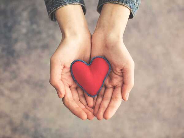 Två händer håller fram ett rött hjärta i tyg.