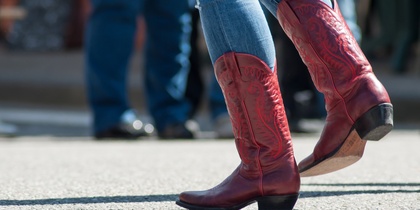 Person i blå jeans och röda cowboyboots dansar utomhus på asfalt.
