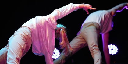 Två personer utför en modern dansrörelse på scen med färgglad belysning.