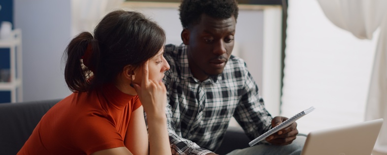 Två personer sitter i ett vardagsrum och tittar koncentrerat på en bärbar dator.