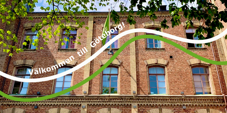 Tegelbyggnad med stora fönster, gröna trädgrenar och texten 'Välkommen till Göteborg!'.