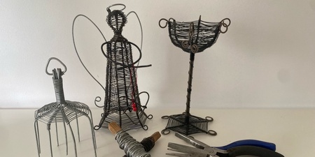 Tre skulpturer av ståltråd, två rullar ståltråd och två tänger på ett vitt bord.
