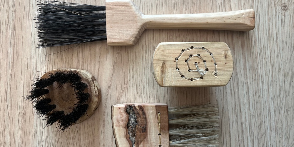 Fyra handgjorda borstar av trä och naturborst ligger på ett ljust trägolv.