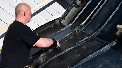 En person arbetar med att lägga takplåt och tätning på ett tak utomhus i dagsljus.