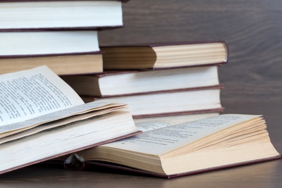 Flera böcker ligger och staplas på ett träbord, några är öppna och andra stängda.