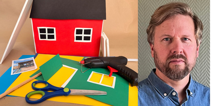 En man med skägg och blå skjorta bredvid ett pysselbord med färgat papper, sax, lim och en modell av ett rött hus.