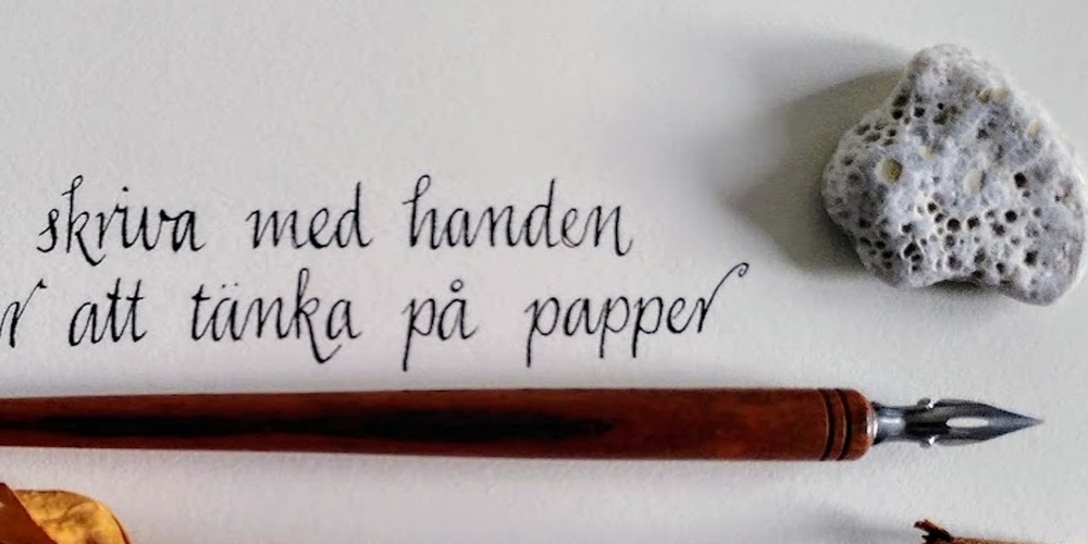 En handskriven svensk text på papper med en gammal bläckpenna, en torkad ros och en sten bredvid.