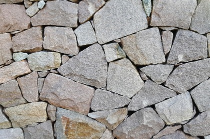 Närbild av en mur byggd av oregelbundna naturstenar i olika storlekar och färger.