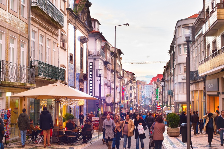 En livlig gågata i en europeisk stad med människor som promenerar och sitter på uteserveringar.