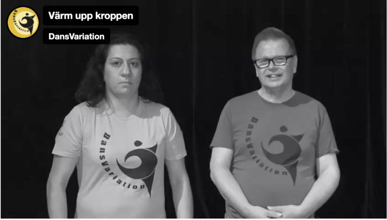 Två personer står bredvid varandra i t-shirts med texten 'Dansvariation' mot en mörk bakgrund.
