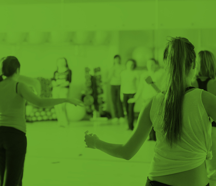 En grupp människor deltar i en träningsklass inomhus, fotograferade bakifrån. Bilden har grön färgton.