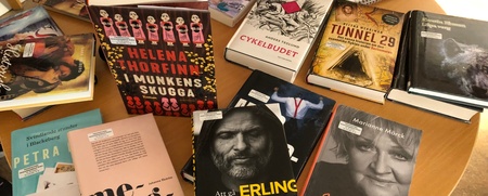 Ett runt bord med flera böcker i olika färger och genrer, samt anteckningsblock och glas vatten.