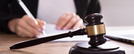 En domarklubba ligger på ett skrivbord medan en person skriver på papper i bakgrunden.