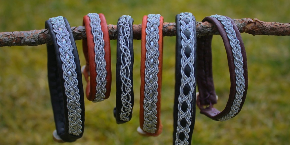 Sex armband med flätade mönster hänger på en gren utomhus med gräs i bakgrunden.