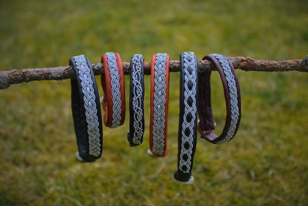 Sex armband med flätade mönster hänger på en gren utomhus med gräs i bakgrunden.