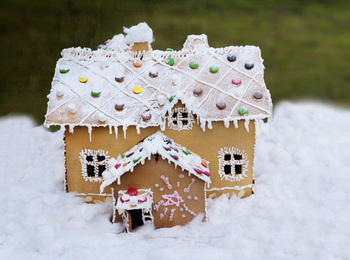 Ett dekorerat pepparkakshus med vit glasyr och färgglada godisbitar står på snö.