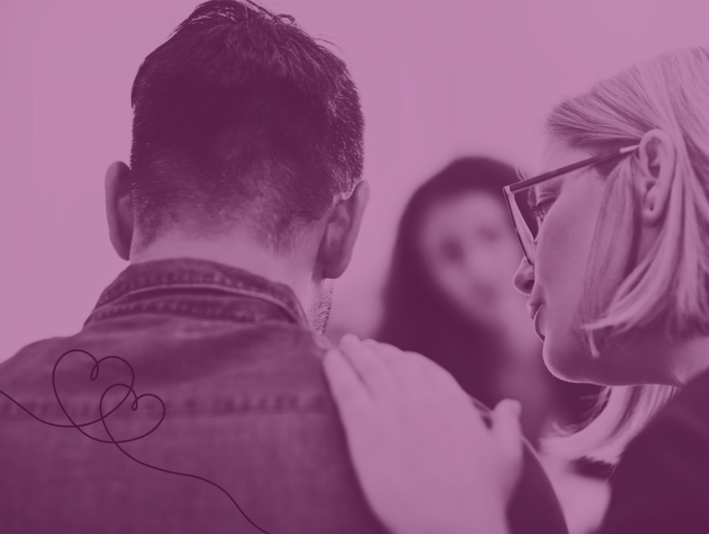 En person lägger en hand på en annans axel i en stödjande gest, med en tredje person i bakgrunden.