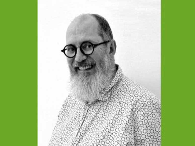 Man med glasögon och skägg ler mot kameran, svartvit bild med grön bakgrund.