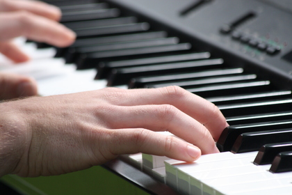 Närbild på händer som spelar på ett svartvitt piano eller keyboard.