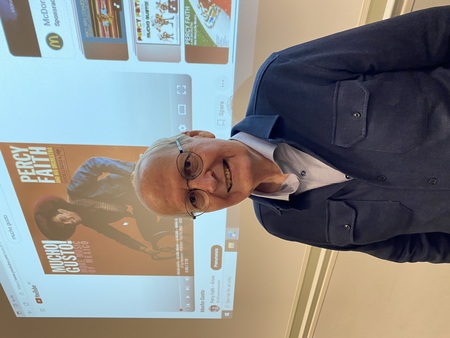 Cirkelledaren Börje Jakobsson står framför en projicerad YouTube-video med Percy Faiths album 'Mucho Gusto' på väggen.