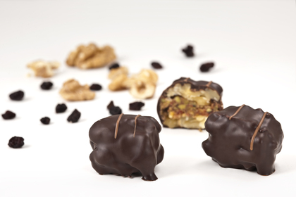 Chokladöverdragna godisbitar med nötter och torkad frukt på vit bakgrund.