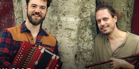 Två män står framför ett träd, en håller ett dragspel och den andra en säckpipa.