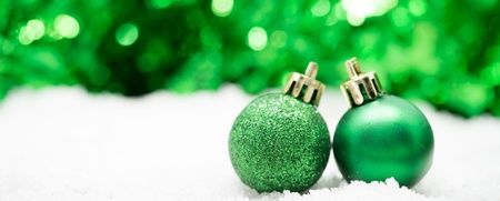 Två gröna julgranskulor står på konstsnö med suddig grön bakgrund.