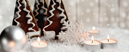 Juldekoration med pepparkaksträd, tända värmeljus, silverkula och snöflinga på konstsnö.