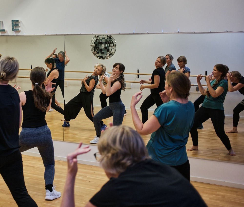 En grupp kvinnor deltar i en dans- eller träningsklass framför en spegelvägg i en dansstudio.
