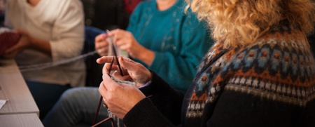 Tre kvinnor sitter tillsammans och stickar med garn och stickor i en varm, inomhusmiljö.